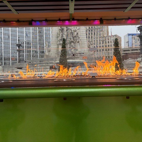 Outdoor fire feature with city buildings and monument visible in the background.